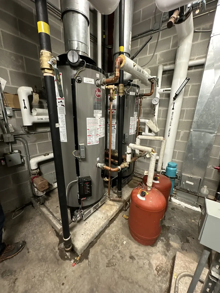 Black gas piping with yellow tags beside a tall water heater, red expansion tanks and white vent pipes in a basement.